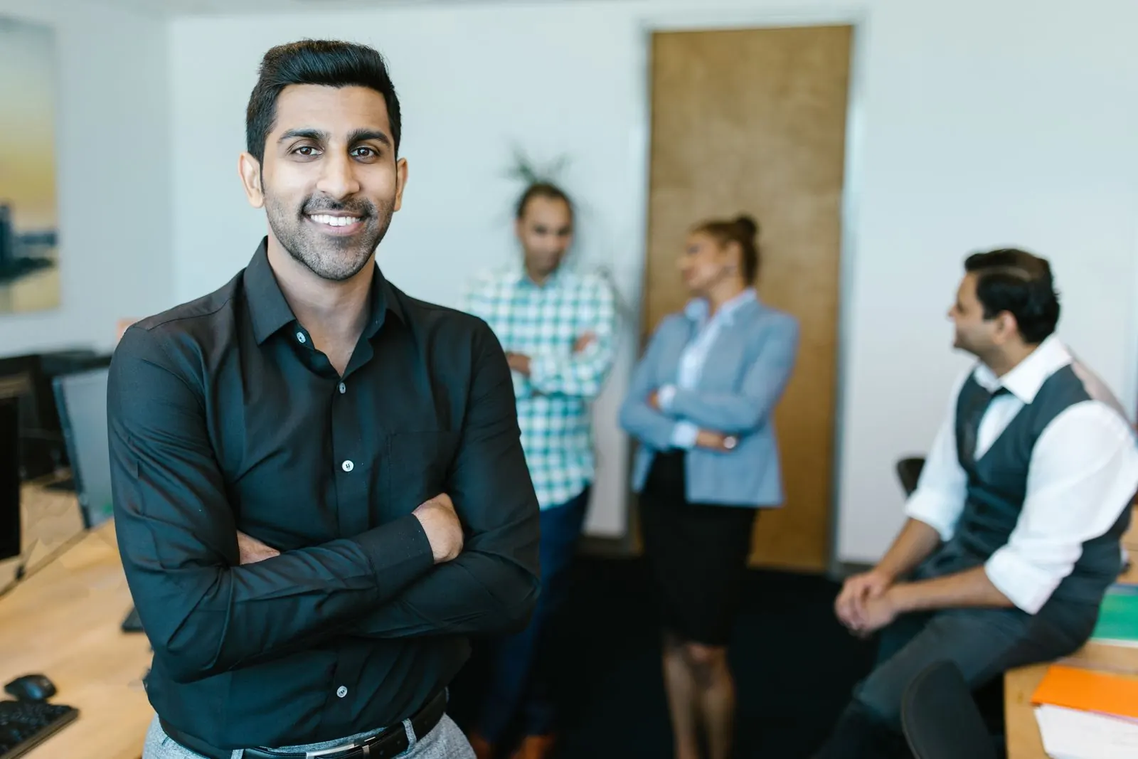 A confident young professional in a modern office with colleagues behind him